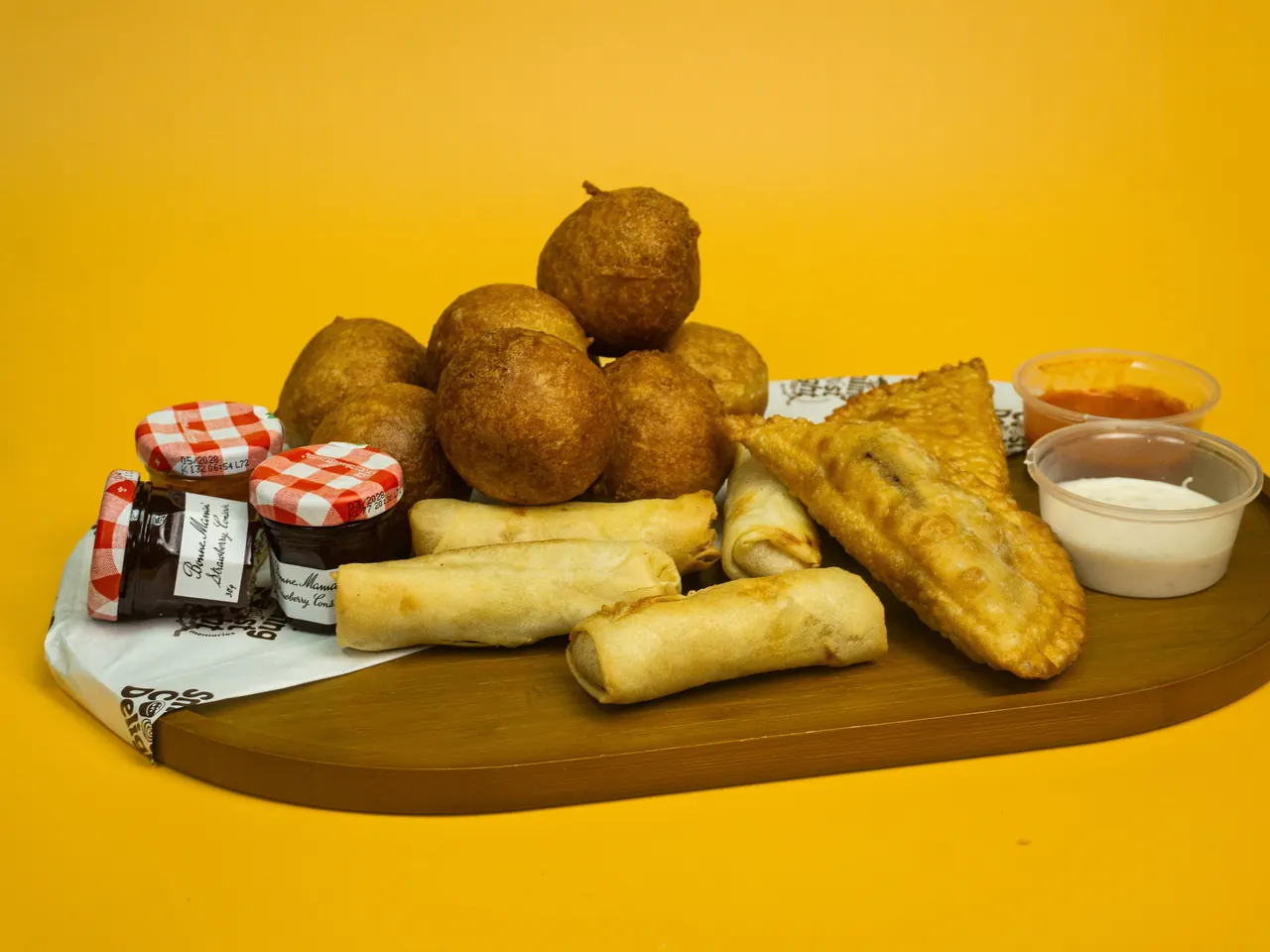 A wooden board of puff puff, spring rolls and pastries with dipping sauces