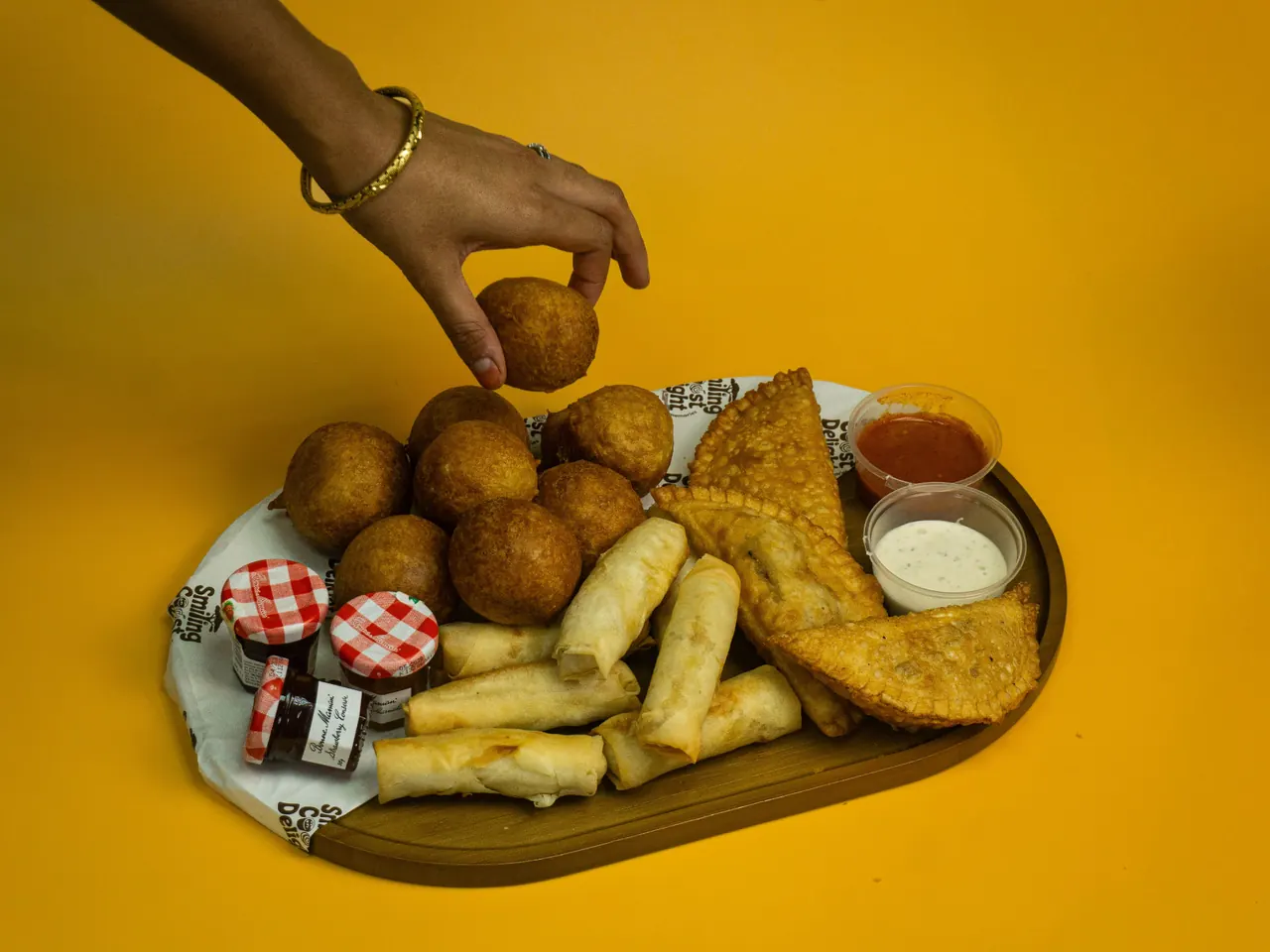 A hand lifting a puff puff from a wooden board of fried snacks